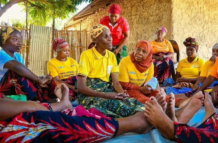 A group of women sit in a circle, listening to an elder speak